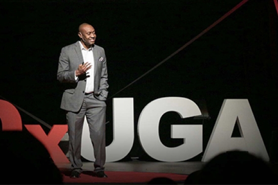 photo of man on stage talking to an audience in foreground