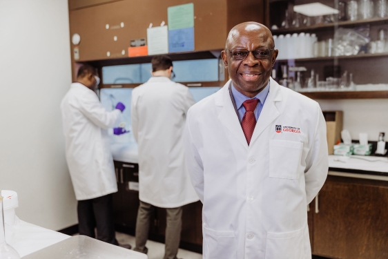 photo of man in lab coat, with two other men in background lab